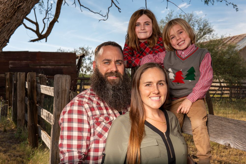 Family portrait by rustic wooden fence with mountains in background.