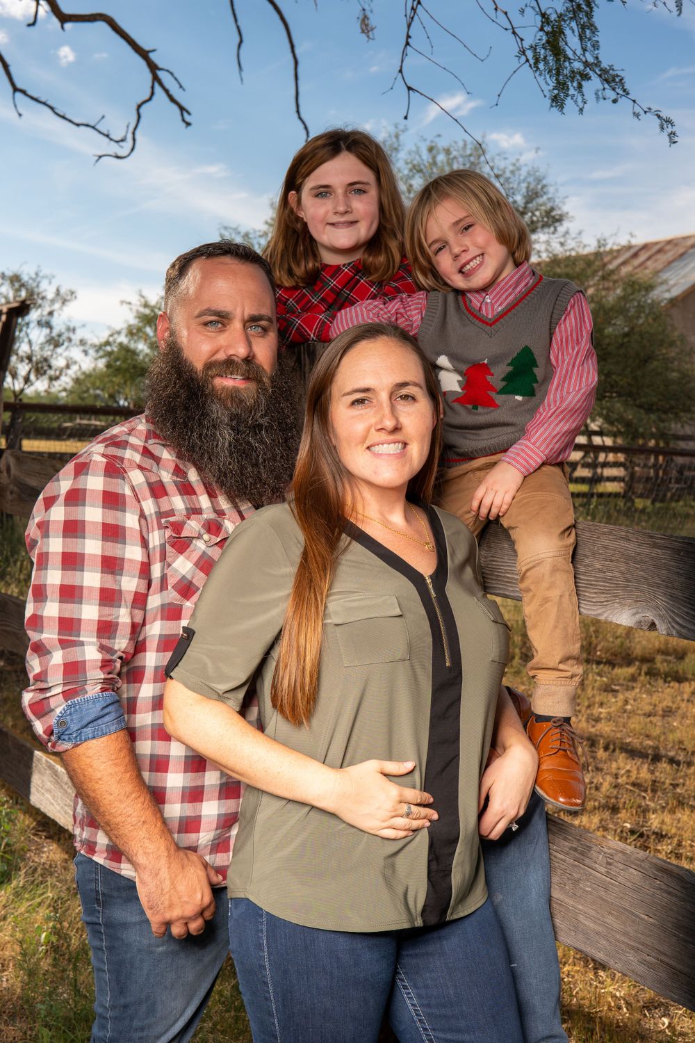 Family group portrait outside with wooden fence and blue sky backdrop.