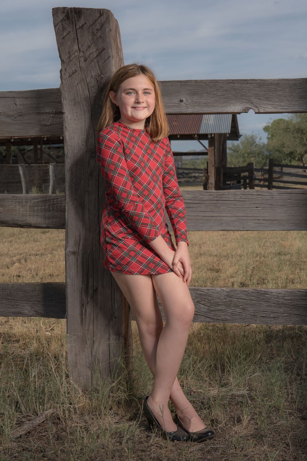 A festive red plaid dress styled for a rustic ranch photoshoot against a wooden fence.