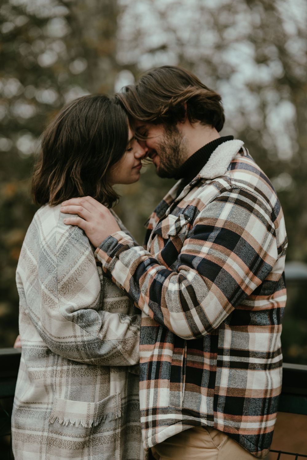 A tender moment between a couple in matching plaid outfits during an autumn photoshoot.