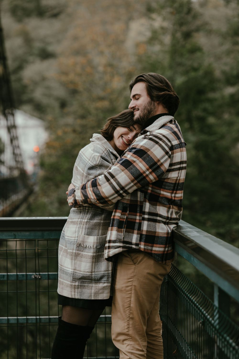 Couple sharing intimate embrace on viewing platform surrounded by autumn trees.