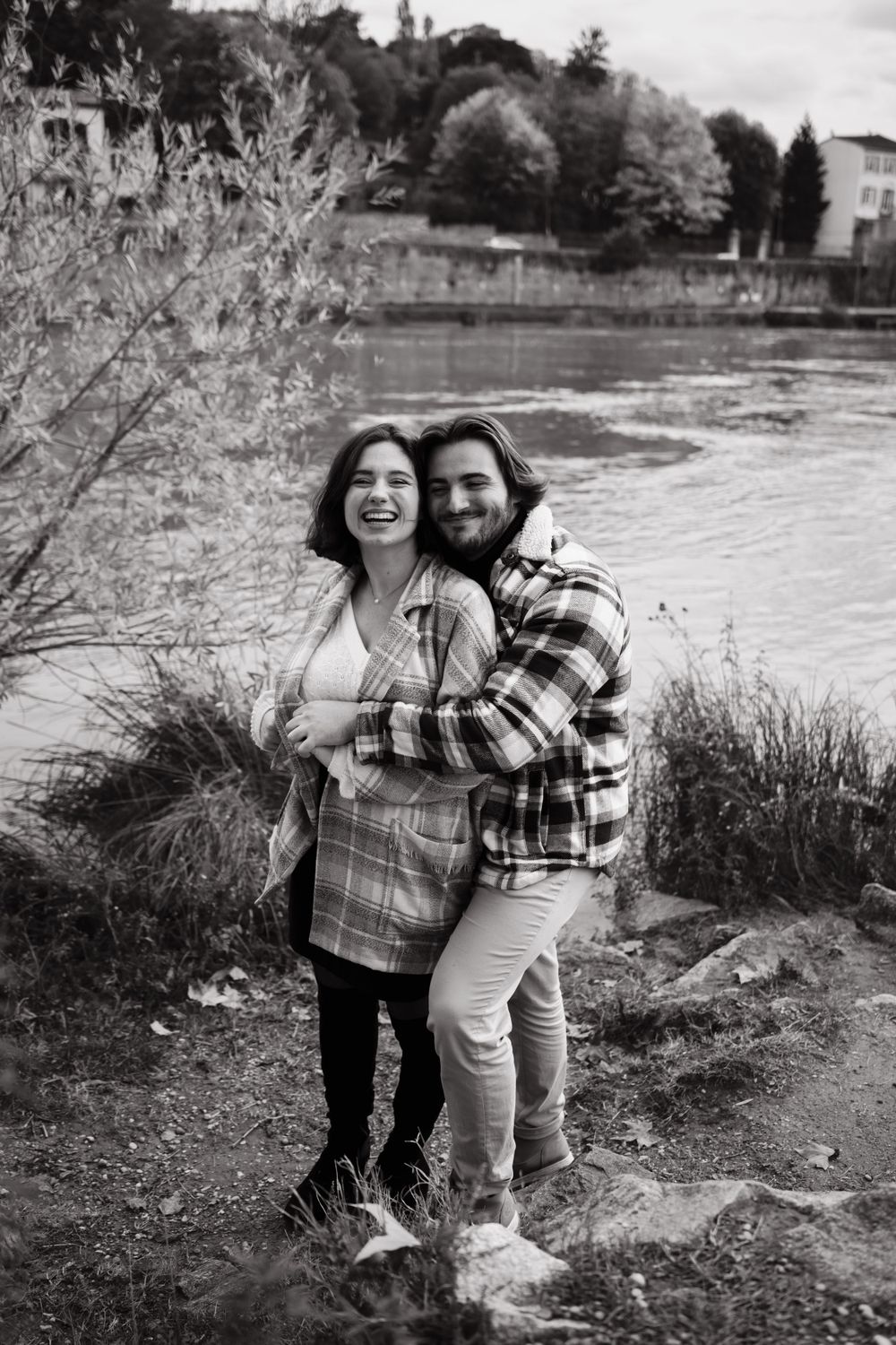 Black and white photo of a happy couple by a lakeside wearing coordinating plaid outfits.
