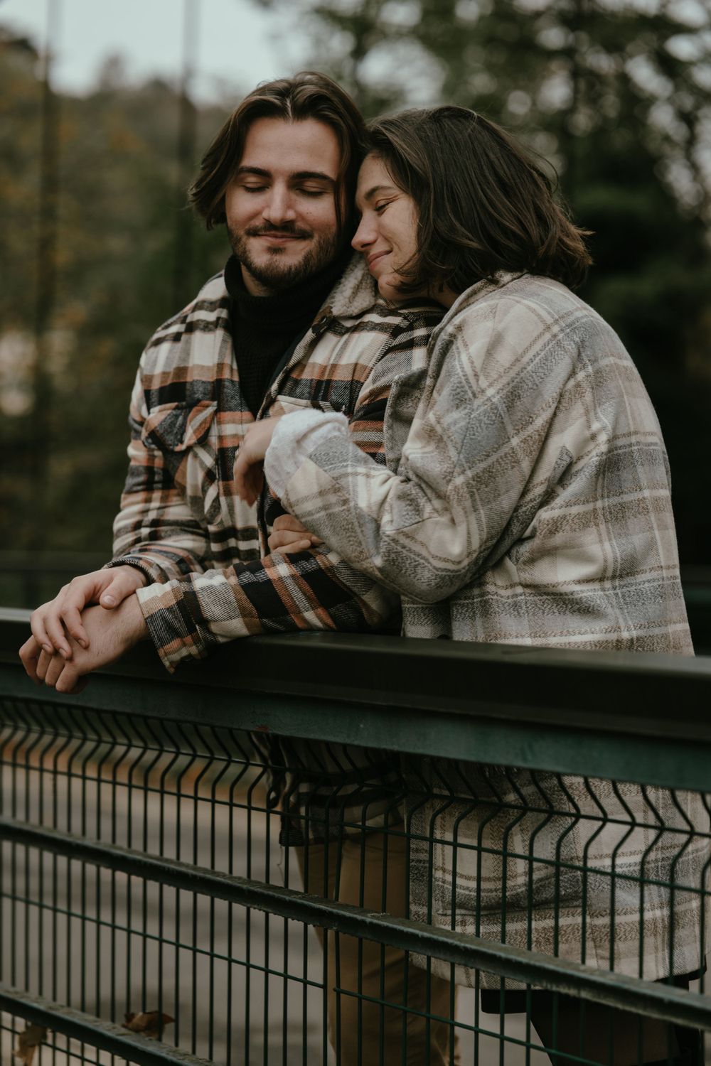 A romantic couple in plaid flannel jackets share an intimate moment on a bridge railing during autumn.