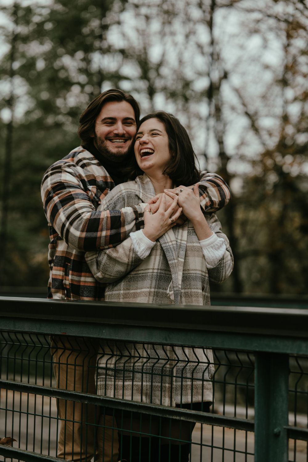 A joyful couple laughing together while wearing cozy plaid jackets outdoors.