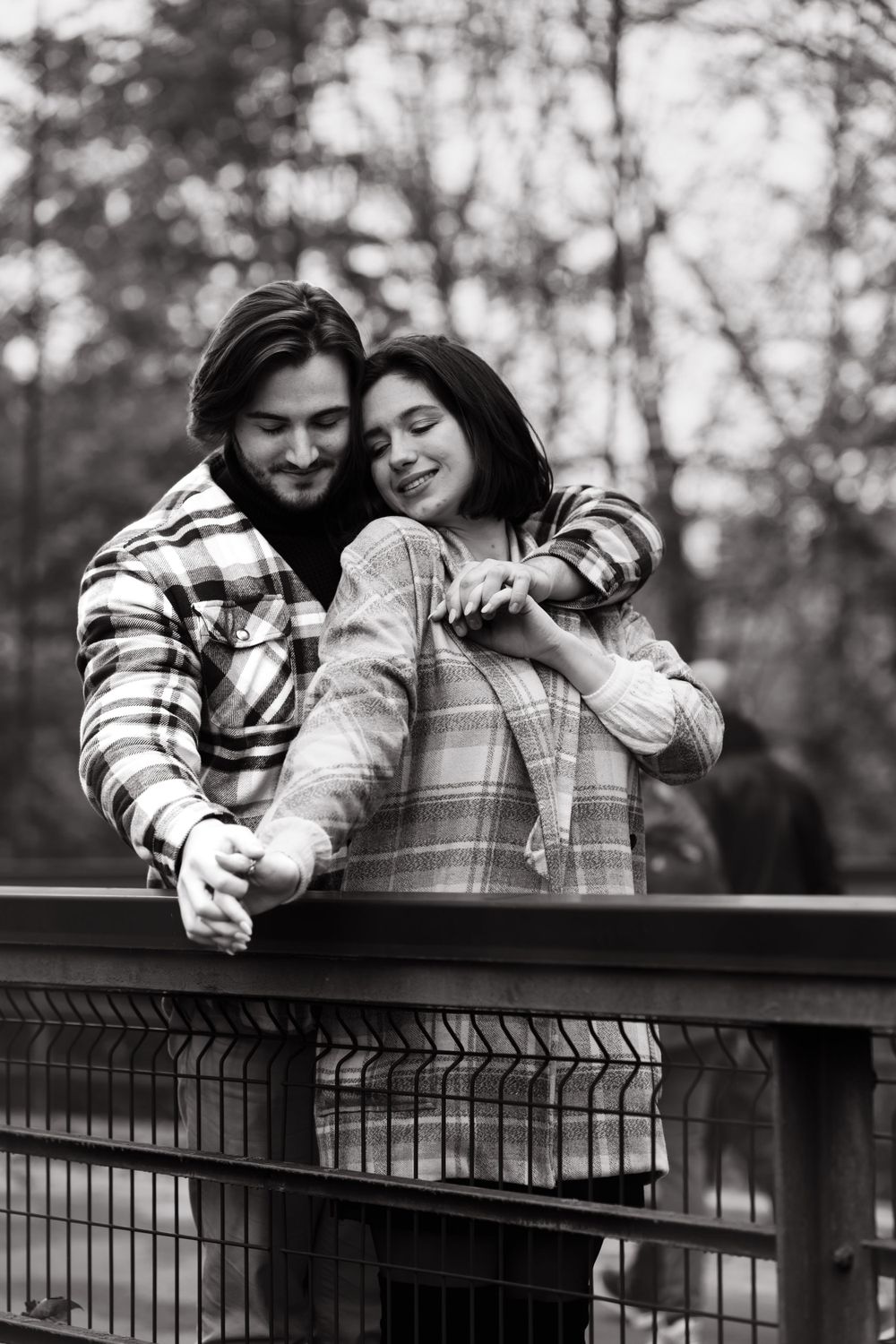 Black and white photo of a couple sharing an affectionate moment on a bridge.
