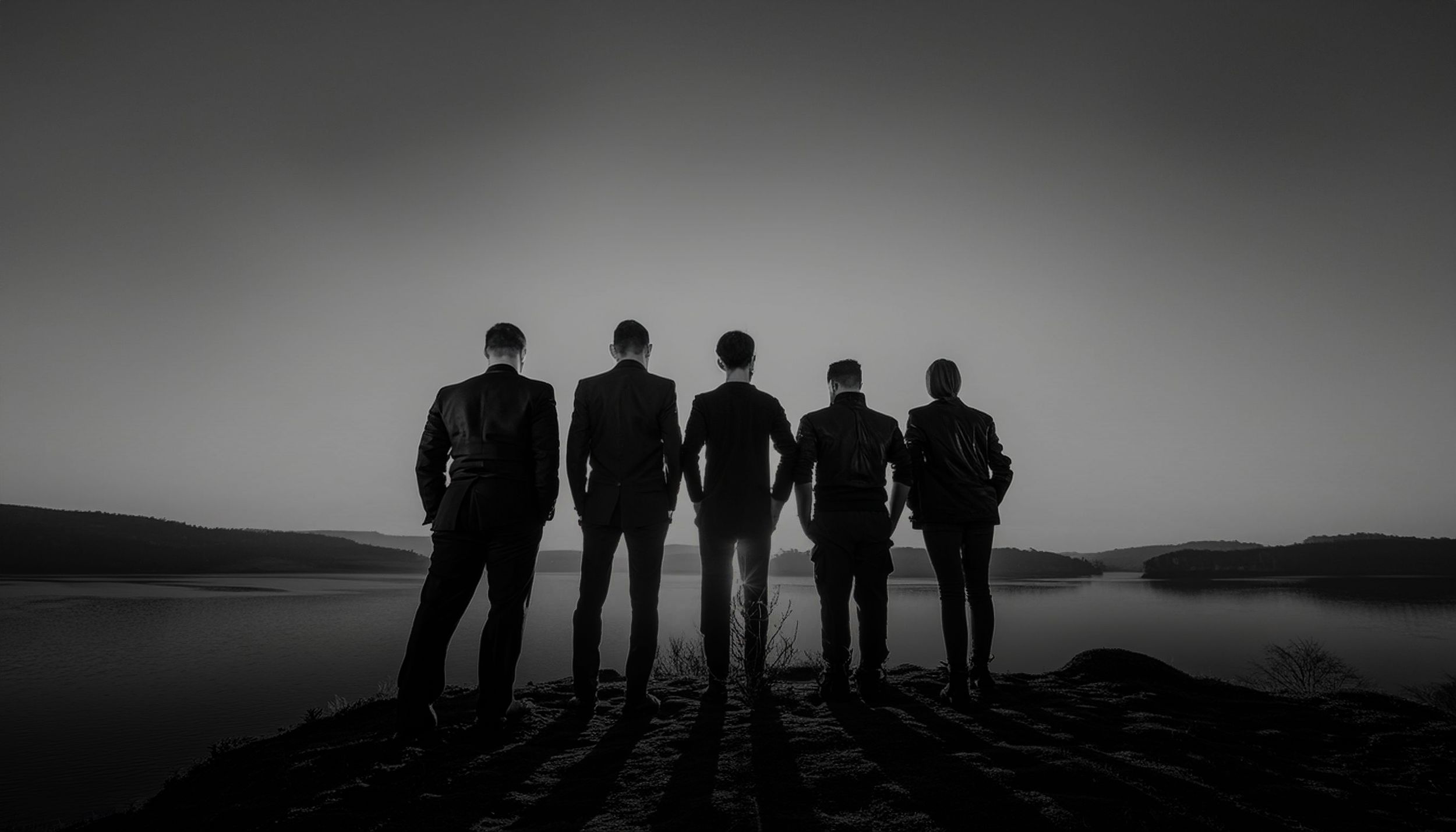 Silhouette of five people standing against dramatic sky and water landscape.