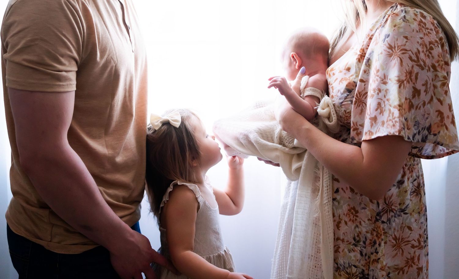 Silhouette of family welcoming newborn baby in backlit indoor setting.