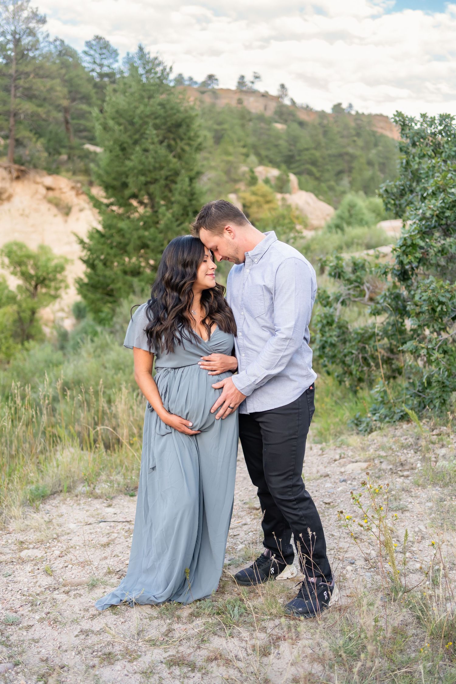 Tender maternity moment shared on a hillside path surrounded by natural greenery.