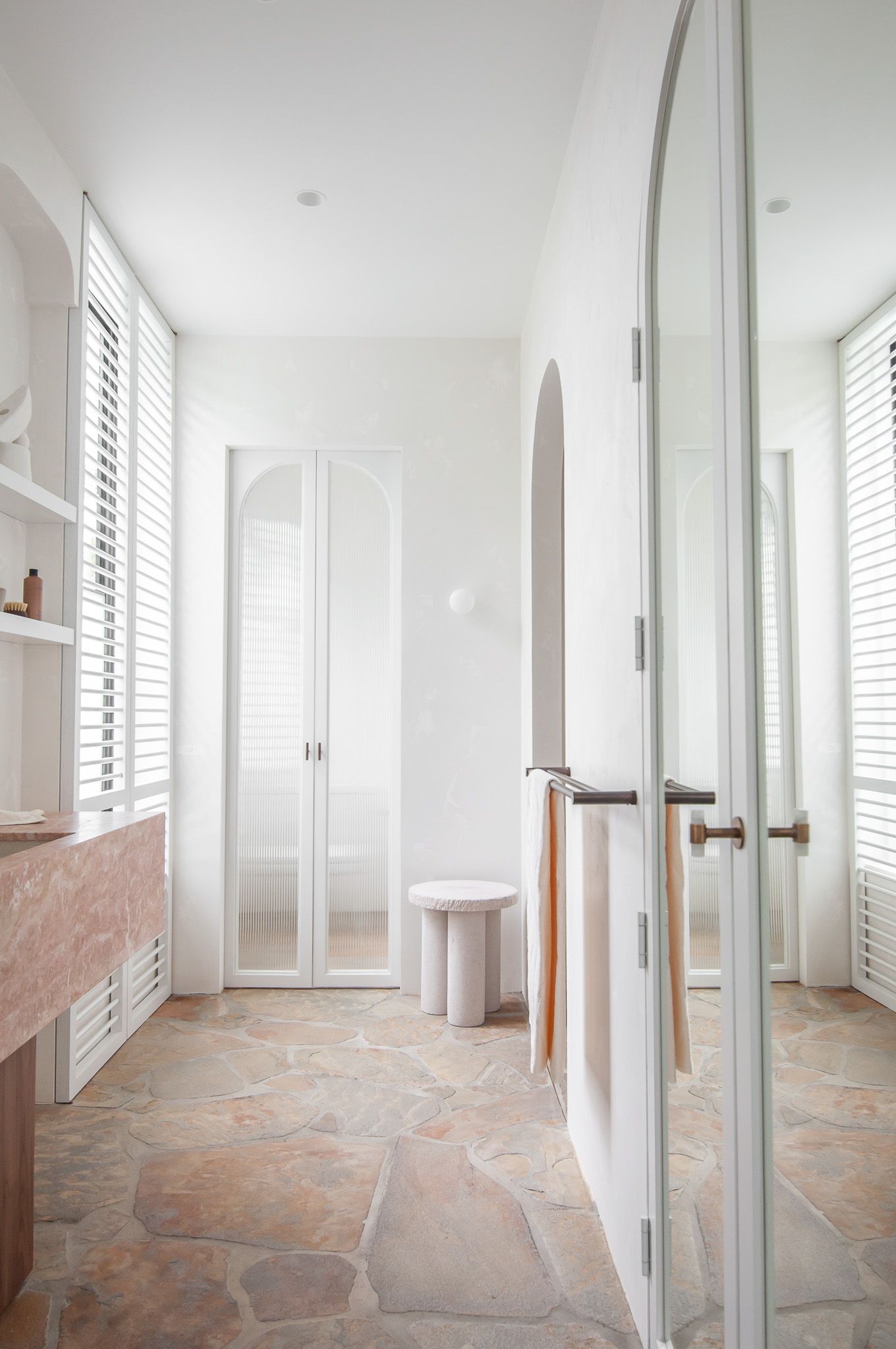 Modern white hallway with arched doorways, stone flooring, and natural light streaming through shuttered windows.