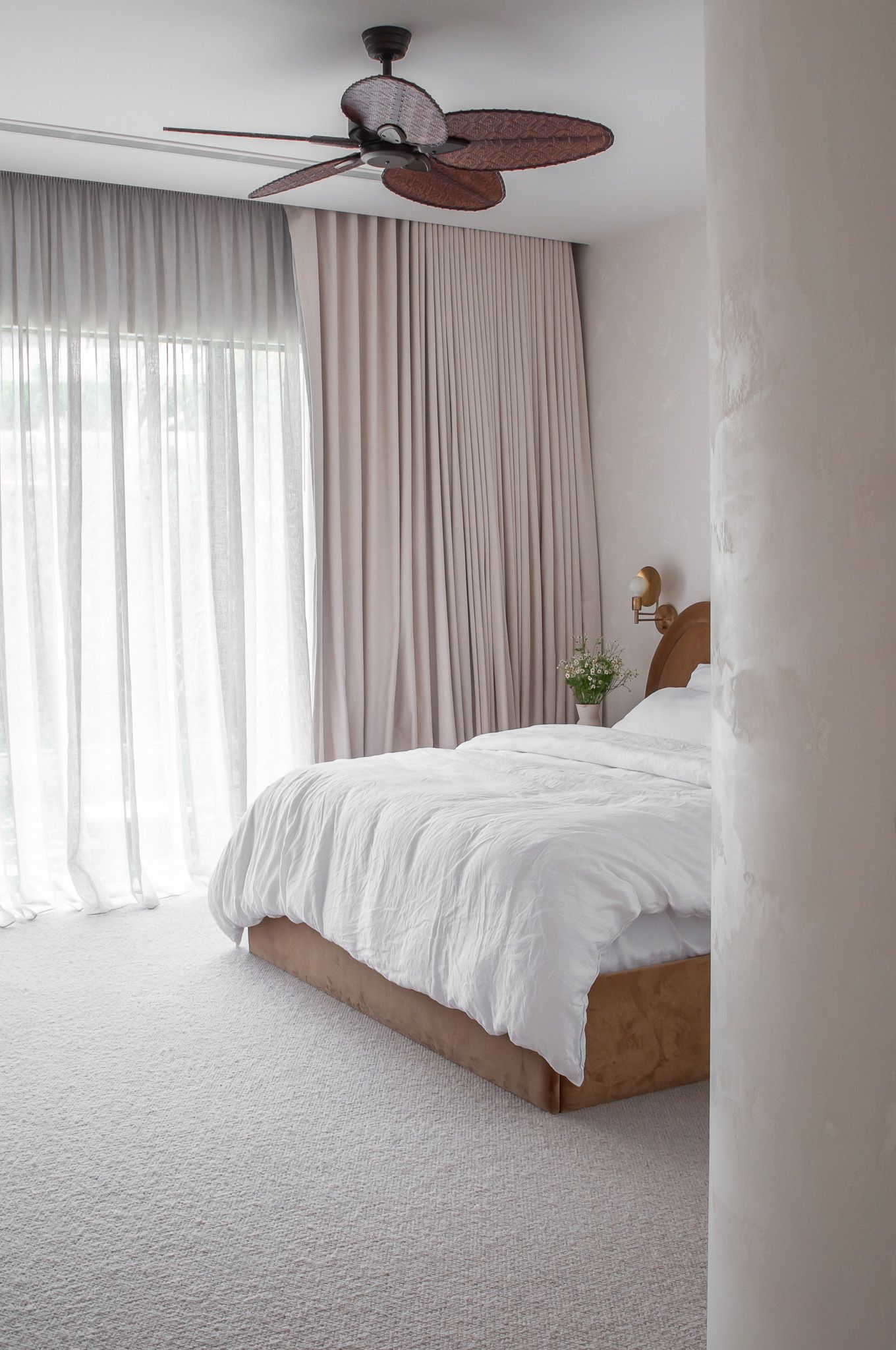 Serene bedroom with white bedding, palm leaf ceiling fan, and floor-to-ceiling curtains.