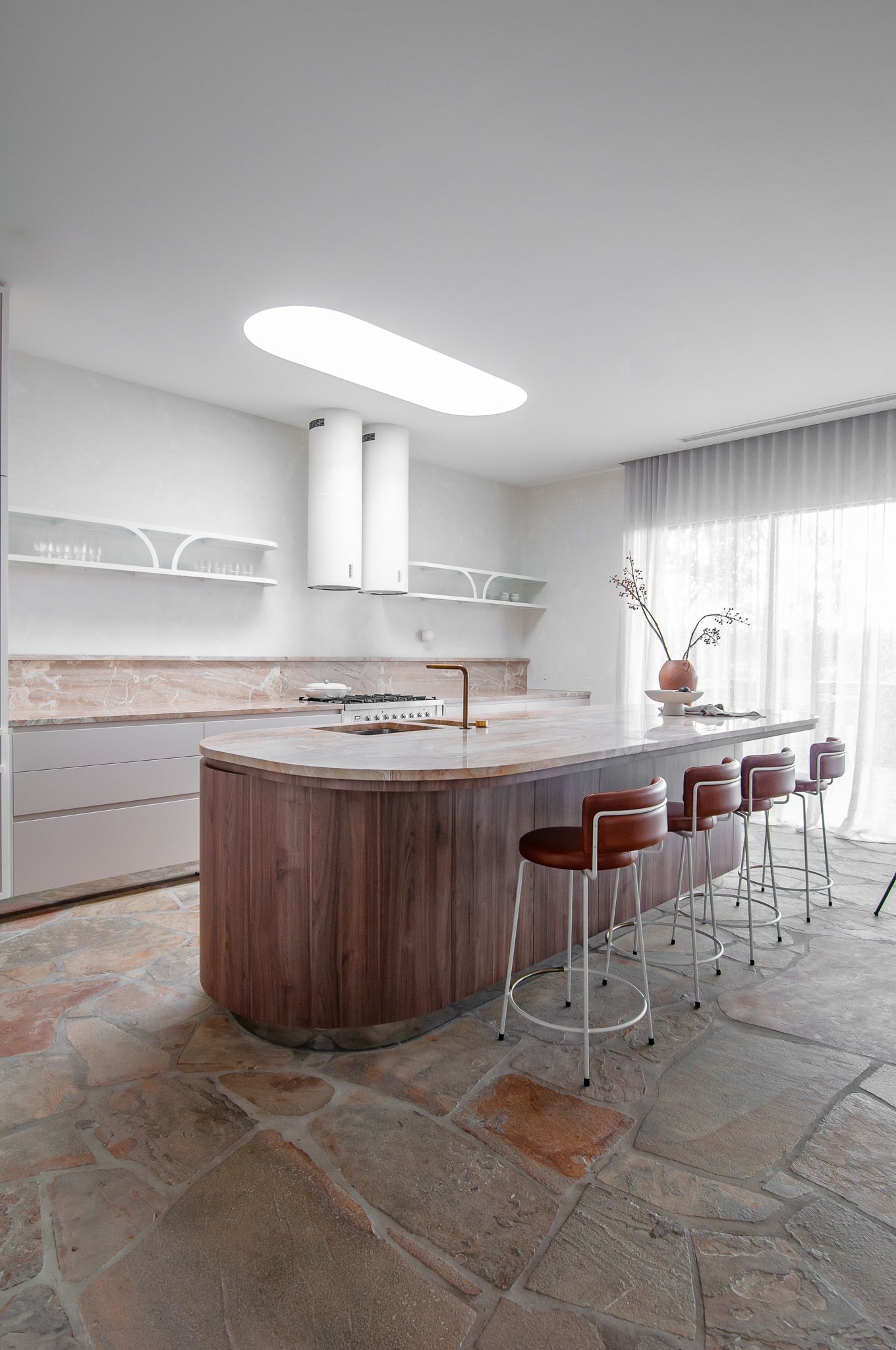 Contemporary kitchen with curved wooden island, leather barstools, and sleek white cabinetry.