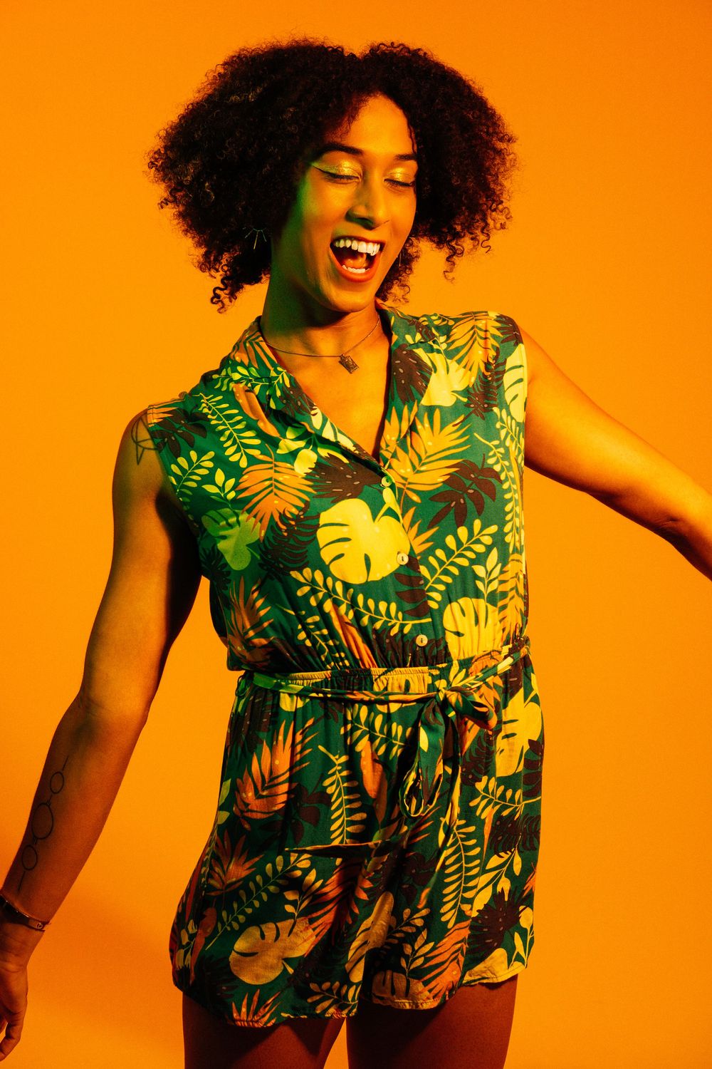 Woman in tropical print dress laughs joyfully against vibrant orange background in dynamic photo series.