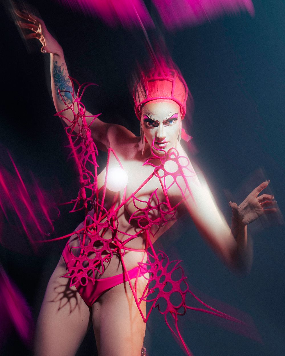 Artistic portrait with pink lighting, dramatic makeup and costume on dark background.