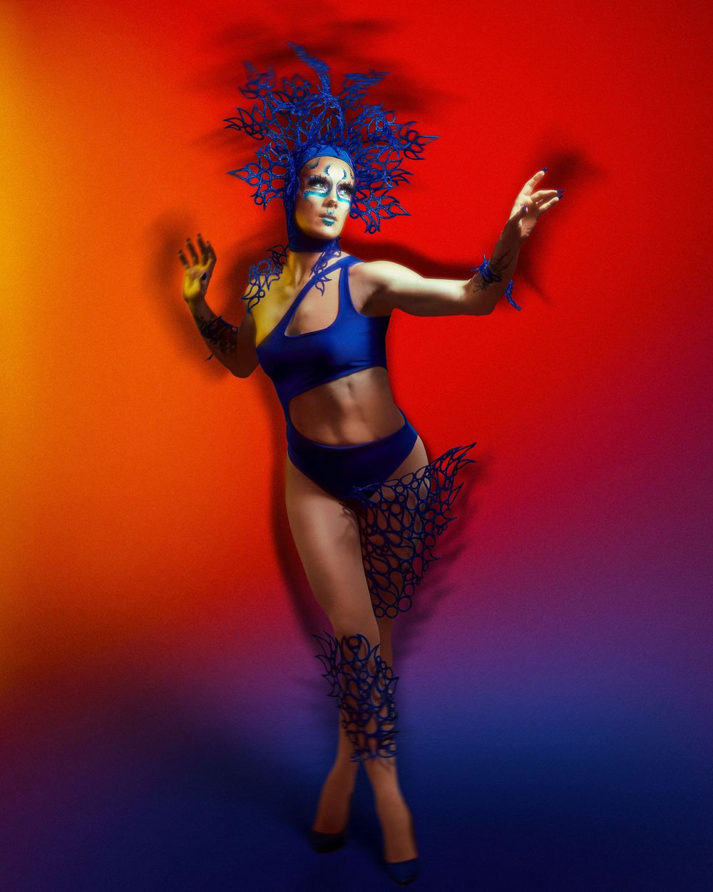 A vibrant photo of a model in a tight blue outfit against a gradient background with shades of reds and purples.