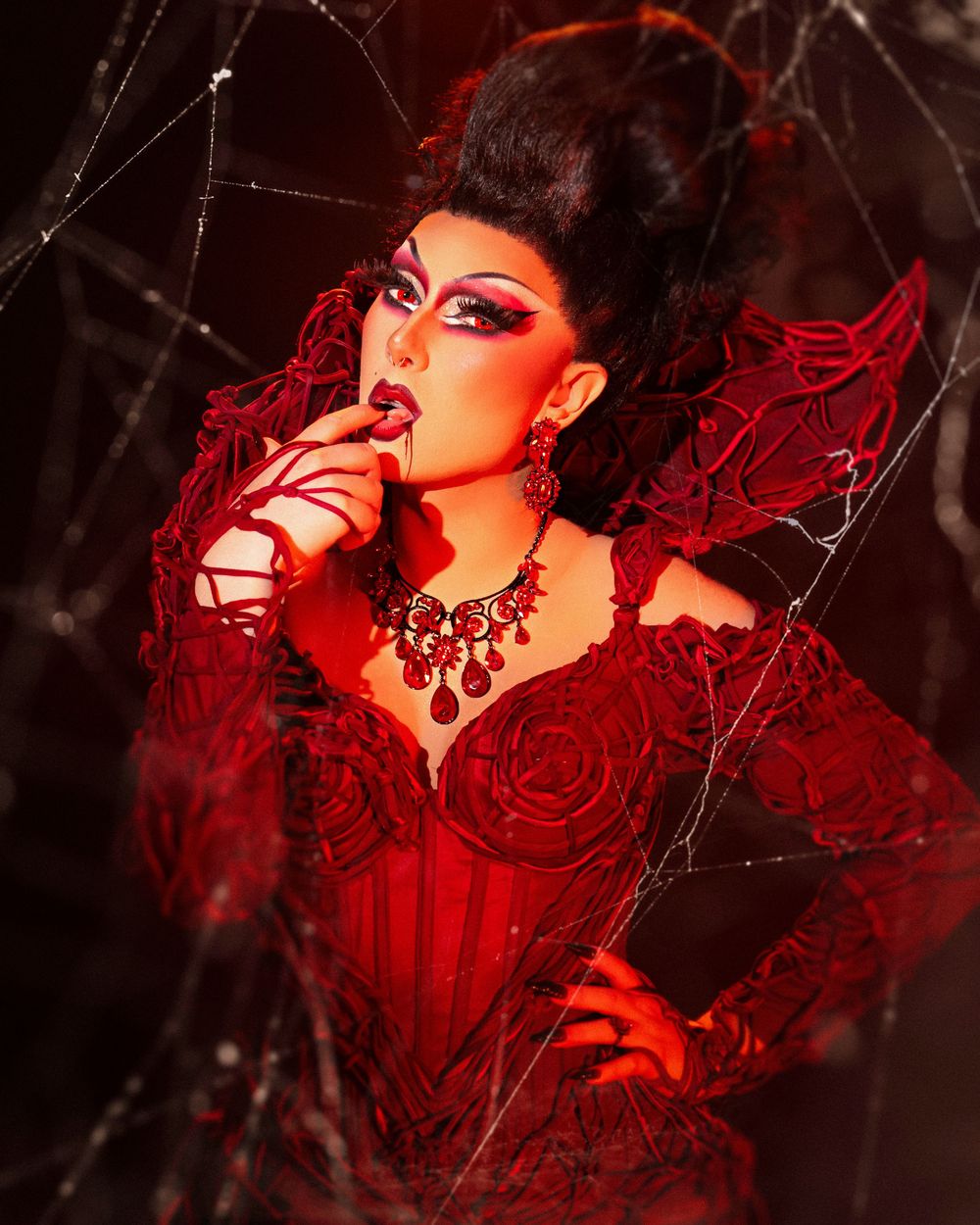 Artistic portrait series in dark red lighting with gothic aesthetic and dramatic makeup against black background.