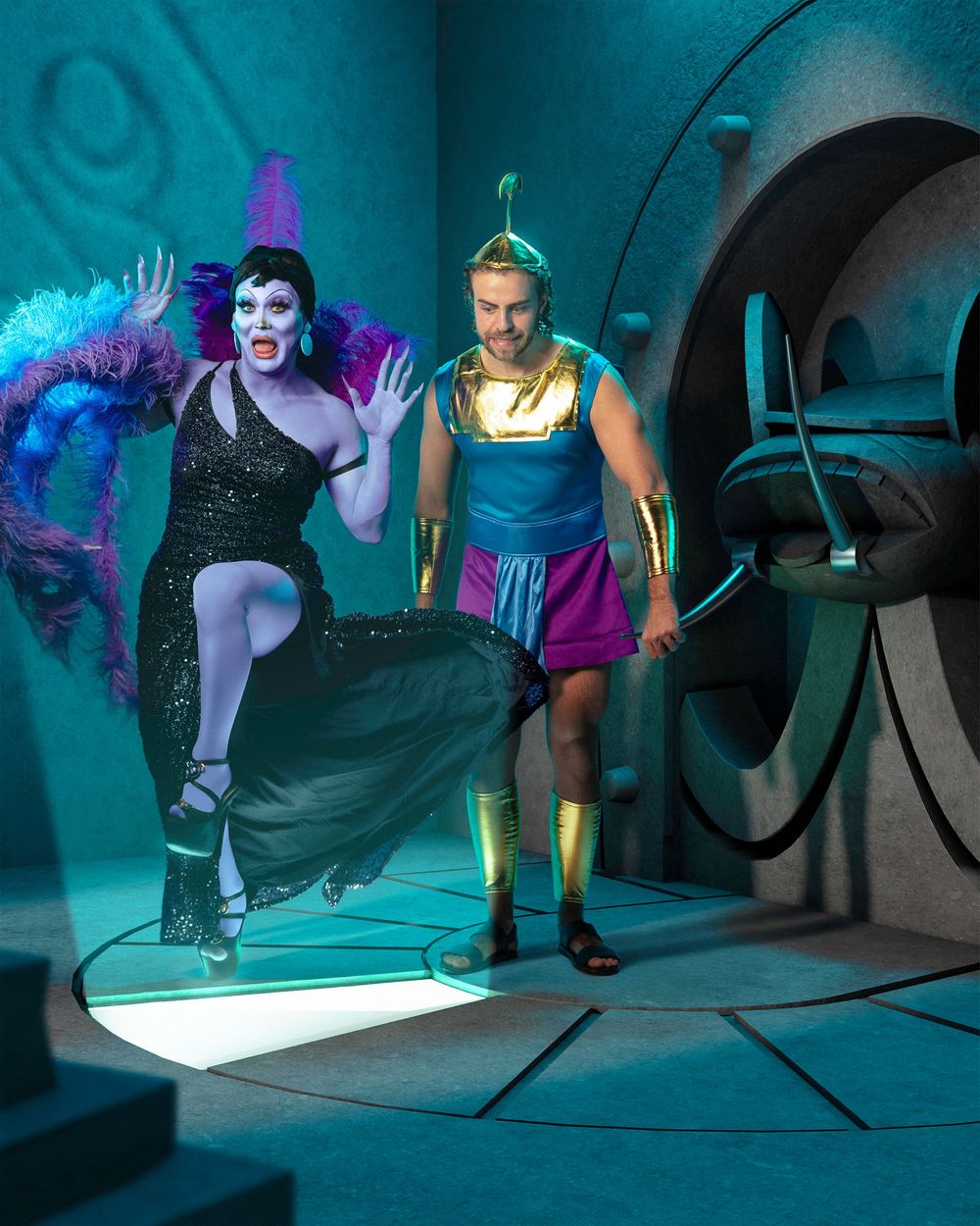 Performers in colorful outfits dance and pose dramatically under turquoise lighting on a stage floor.