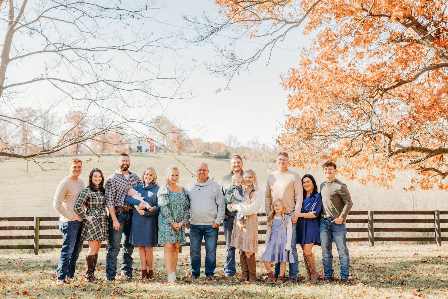 Extended family gathering for outdoor portrait session in autumn setting.