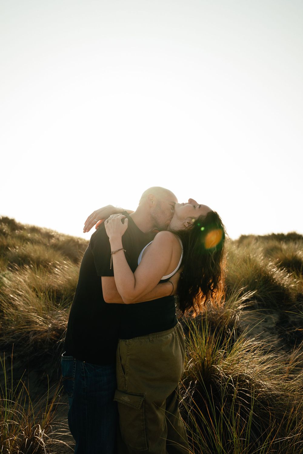 A couple embraces in a romantic silhouette against golden sunlight and tall grass during sunset.