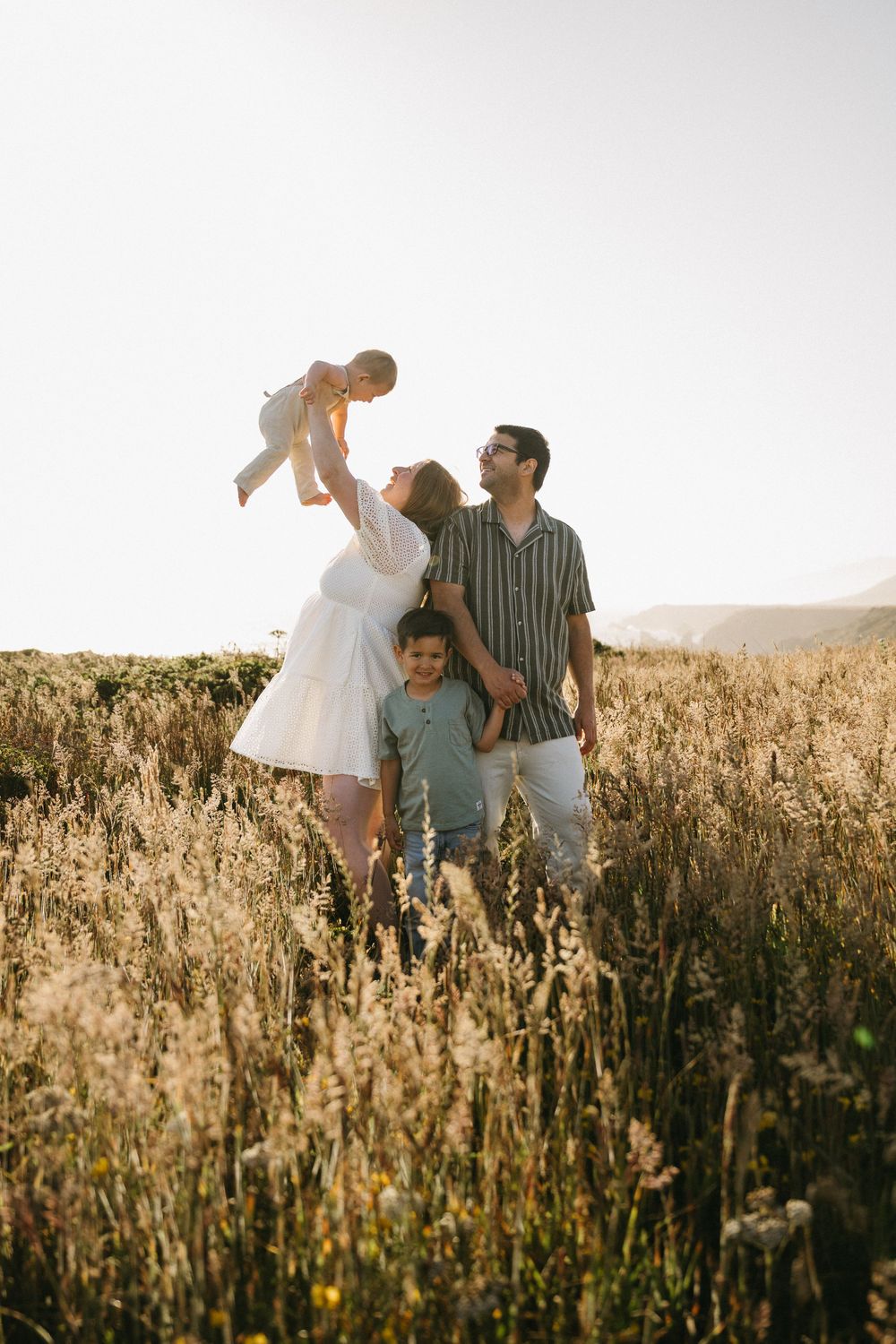 Three people sitting together in a golden meadow during sunset, sharing joyful moments between tall grass.