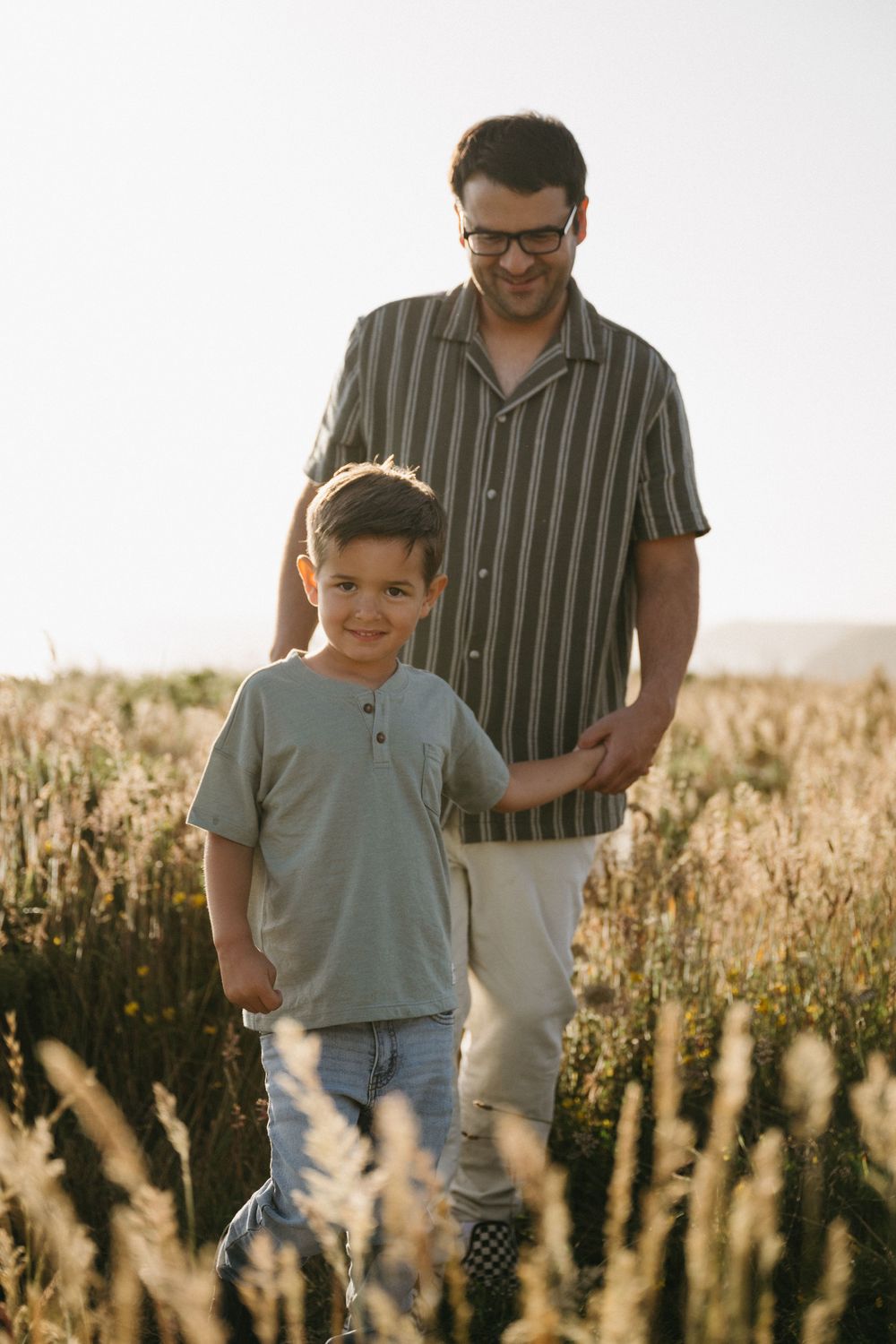 Parent and child walking together through a golden field at sunset creating a heartwarming silhouette.