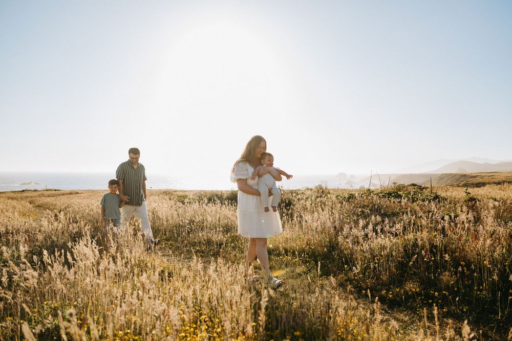 People walking through a golden wheat field at sunset with glowing sunlight creating silhouettes against the horizon.