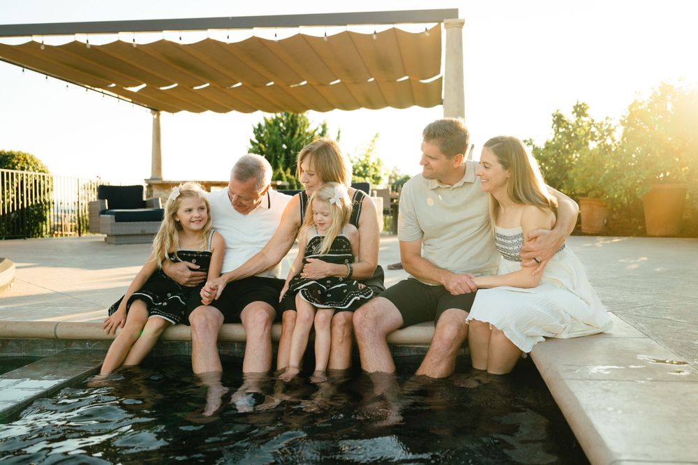A group of people sit together on a concrete ledge at sunset creating a playful summer scene by the pool.