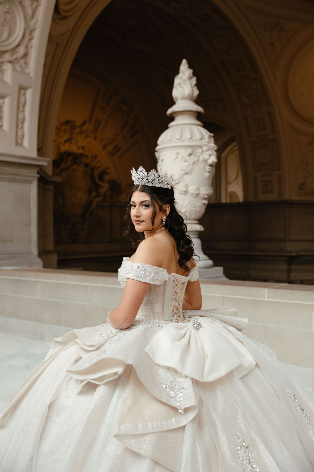 Elegant off-shoulder ball gown with intricate lace corset and full layered skirt photographed in San Francisco City Hall for a Quinceañera .