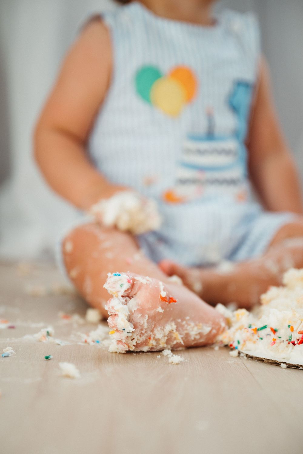 Small hands playing with crumbled cake and colorful sprinkles on a light surface.