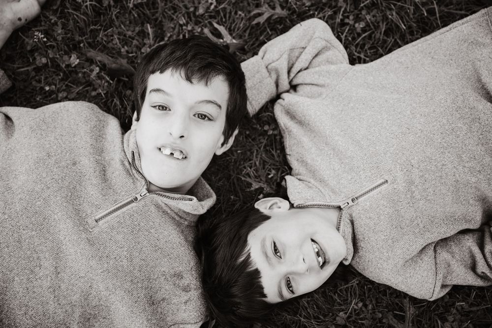 Two children lying on grass wearing sweaters, shot from above in black and white photography.