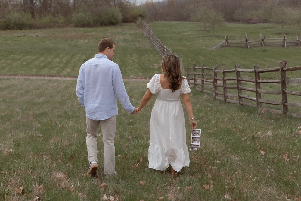Couple walks hand in hand through rustic countryside with wooden fence.