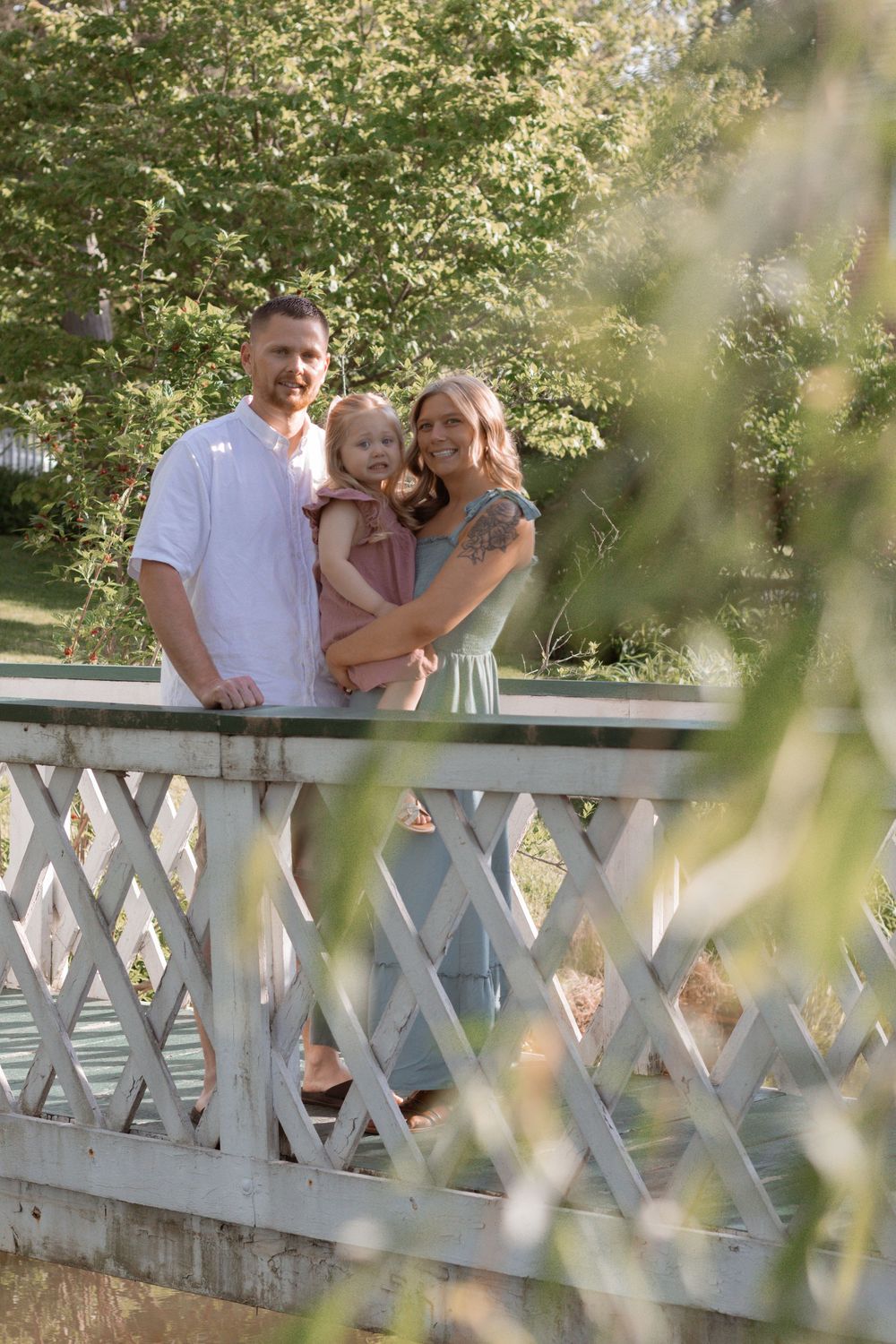 Family enjoying a summer day together on a white latticed bridge in a park setting.