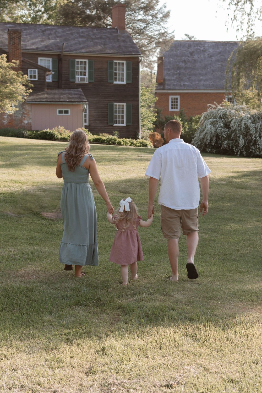 Family walking hand in hand across a lawn with colonial style houses behind them.
