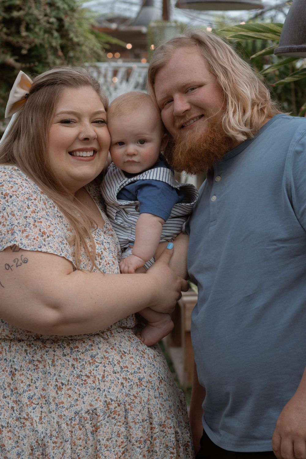 A family portrait captured in a greenhouse with lush plants in the background.