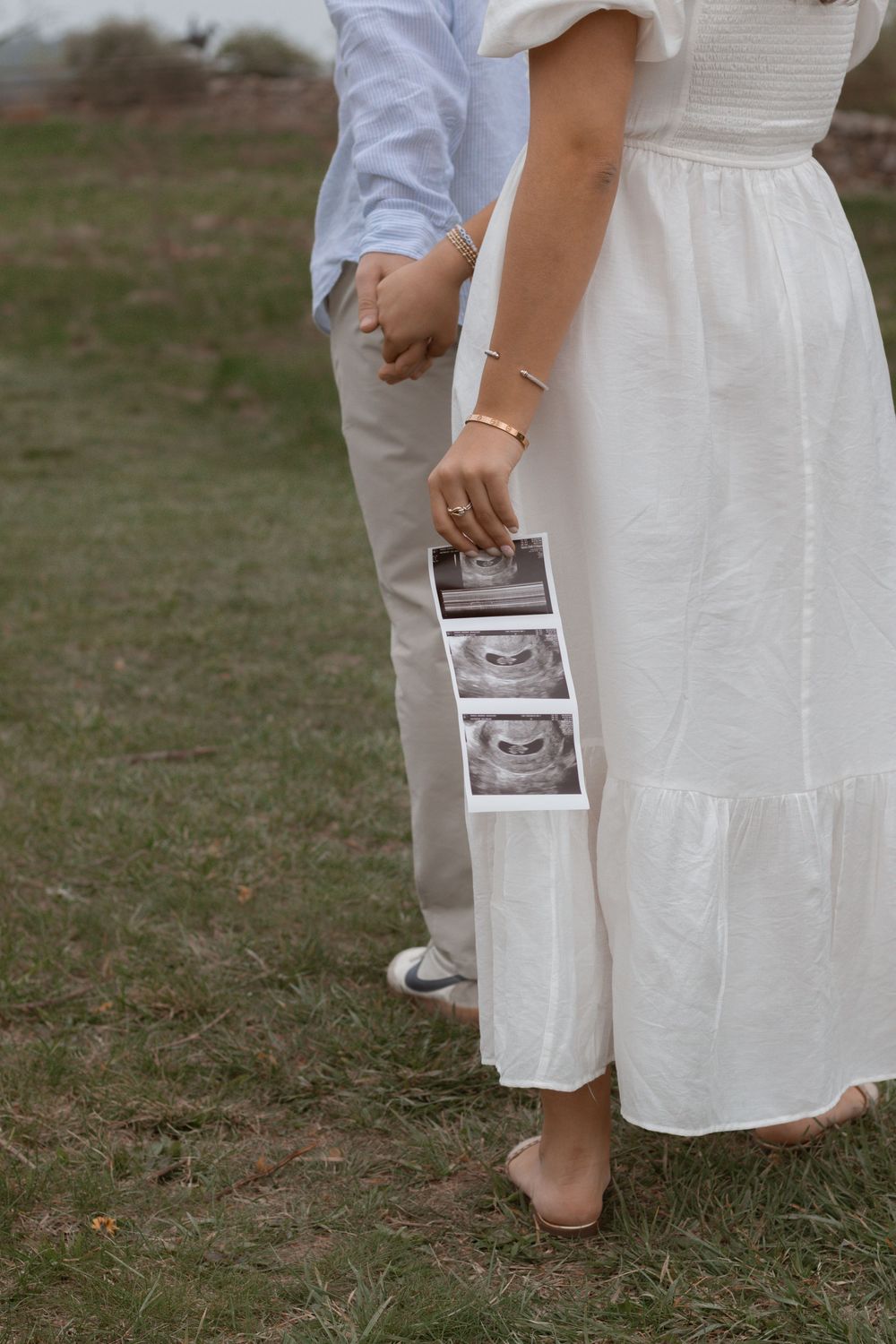 Close-up shot of a couple holding ultrasound photos while wearing coordinated blue and white outfits outdoors.