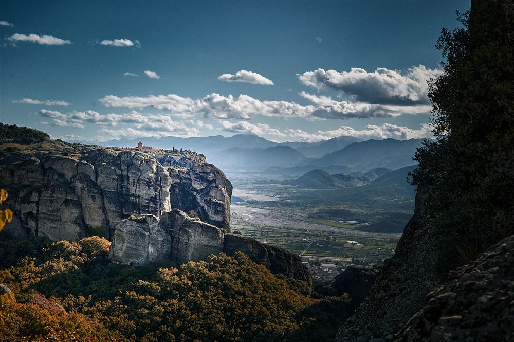 Sweeping landscape of Meteora's dramatic rock pillars and monasteries under a bright blue sky with scattered clouds.