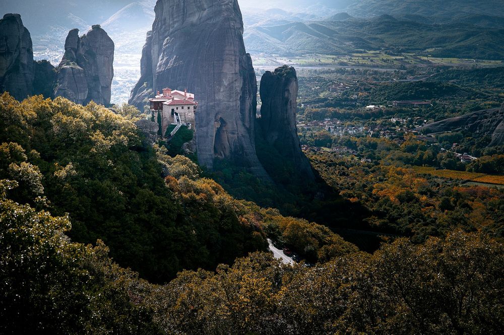 Panoramic view of majestic cliffs and monasteries in Meteora with autumn foliage and mountain backdrop.