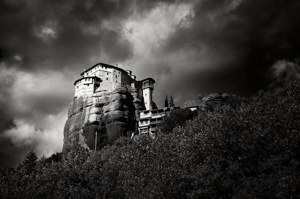 A dramatic black and white landscape shows old buildings silhouetted against stormy skies.