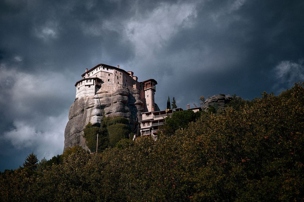 Dramatic stormy sky over ancient stone monasteries perched on towering rock formations in Meteora, Greece.