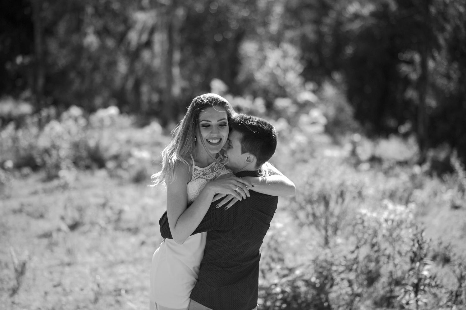 A black and white photo captures a joyful embrace between a couple outdoors.