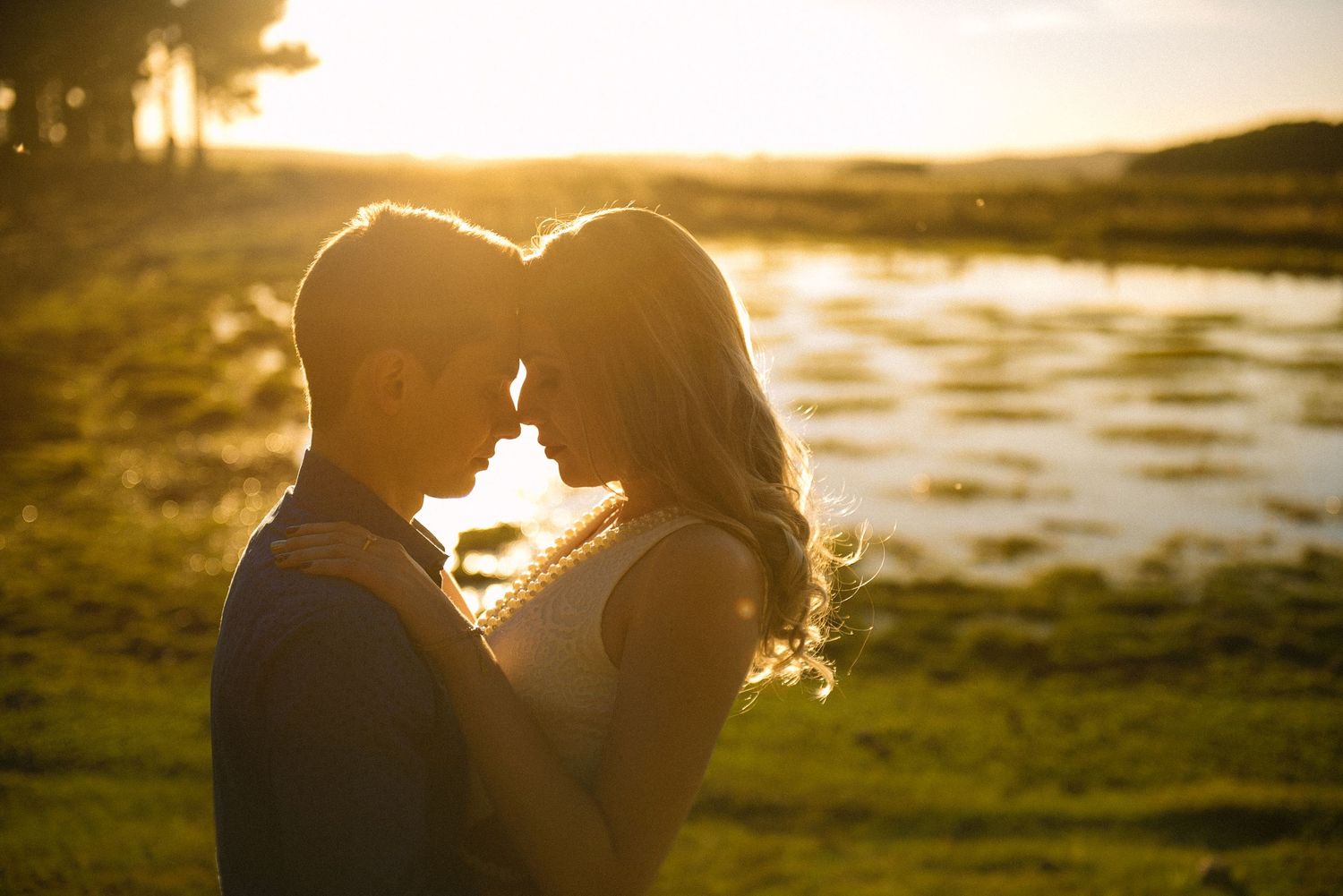 A silhouetted couple sharing an intimate moment against a golden sunset by the water.