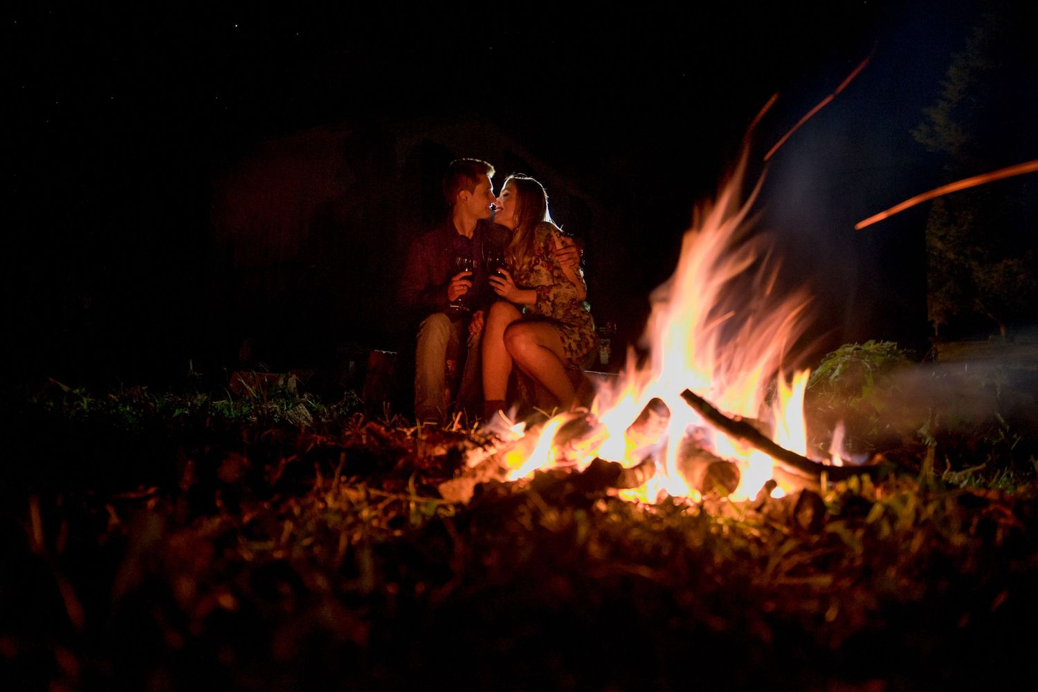 A romantic fireside moment captured in the warm glow of a crackling campfire at night.