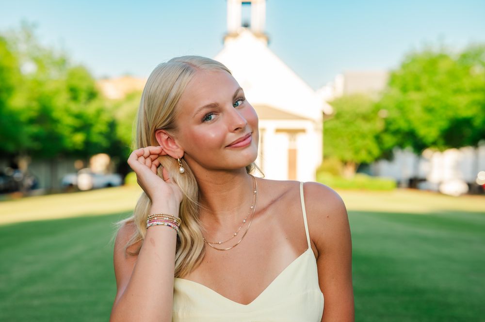 Young blonde woman in yellow dress posing outdoors near a white chapel on a sunny day.