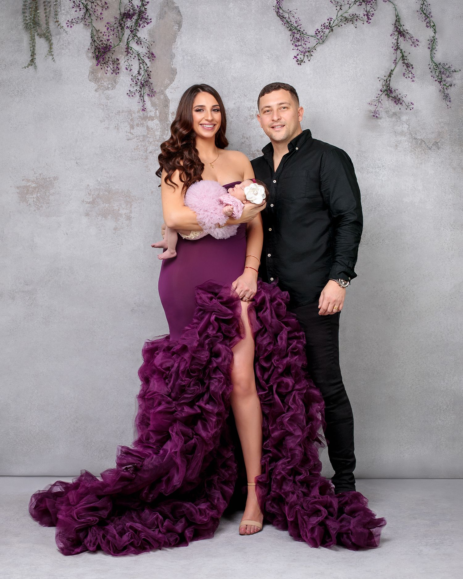Stunning newborn family photo, mother wearing purple couture gown and daughter in matching mauve fluffy dress and white flower headband.