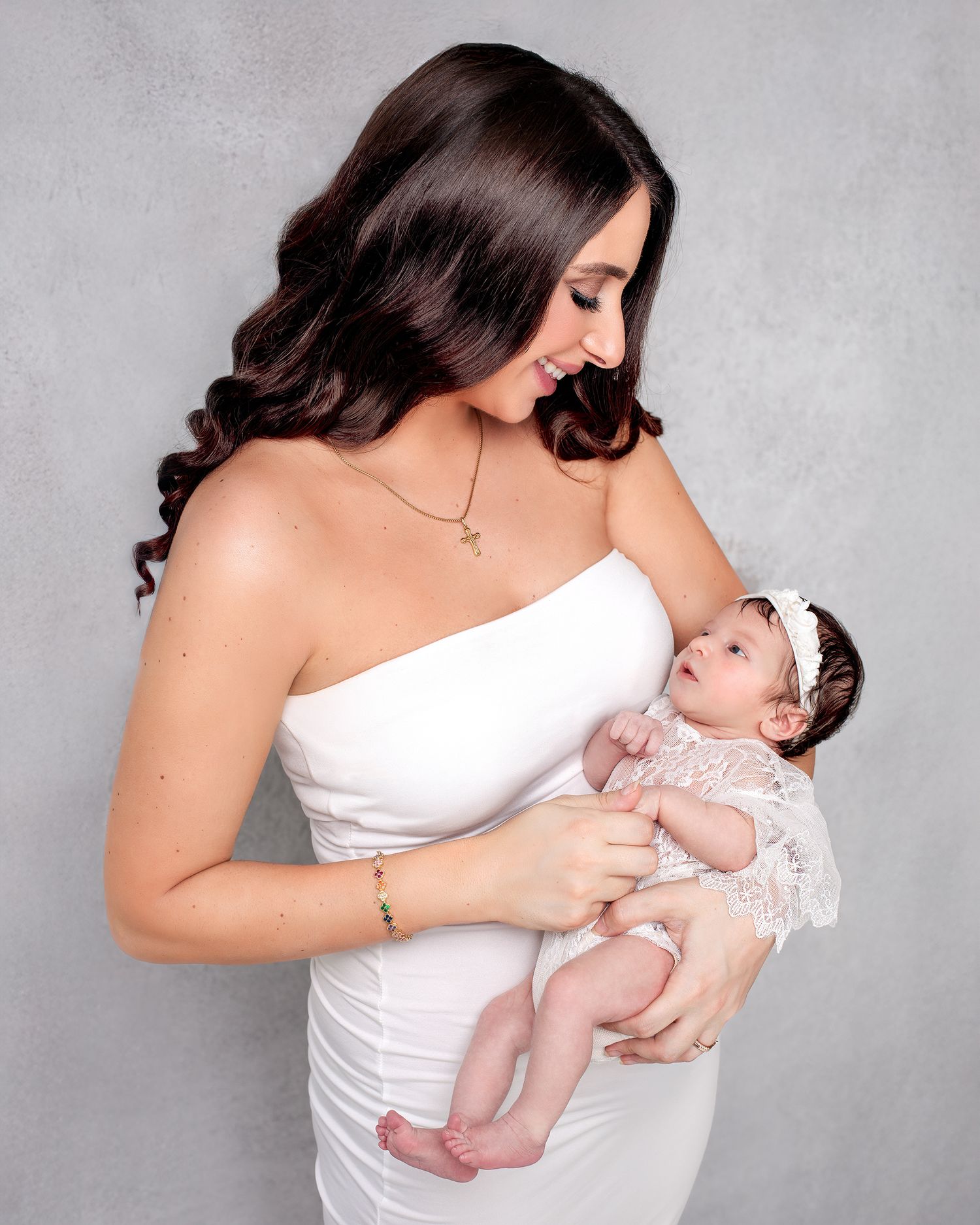 Mother holding newborn baby girl smiling, showing loving connection between mother and daughter. Mother and newborn girl white lace romper