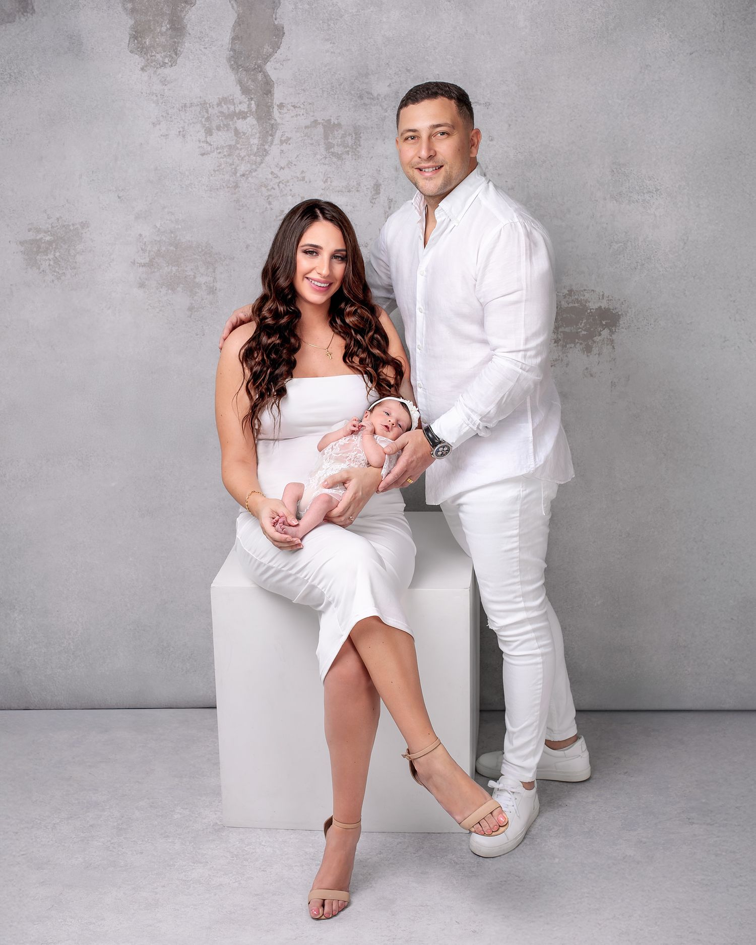 Newborn Family Photo of mother father and newborn baby girl all in matching white clothes. Mother holding newborn smiling.