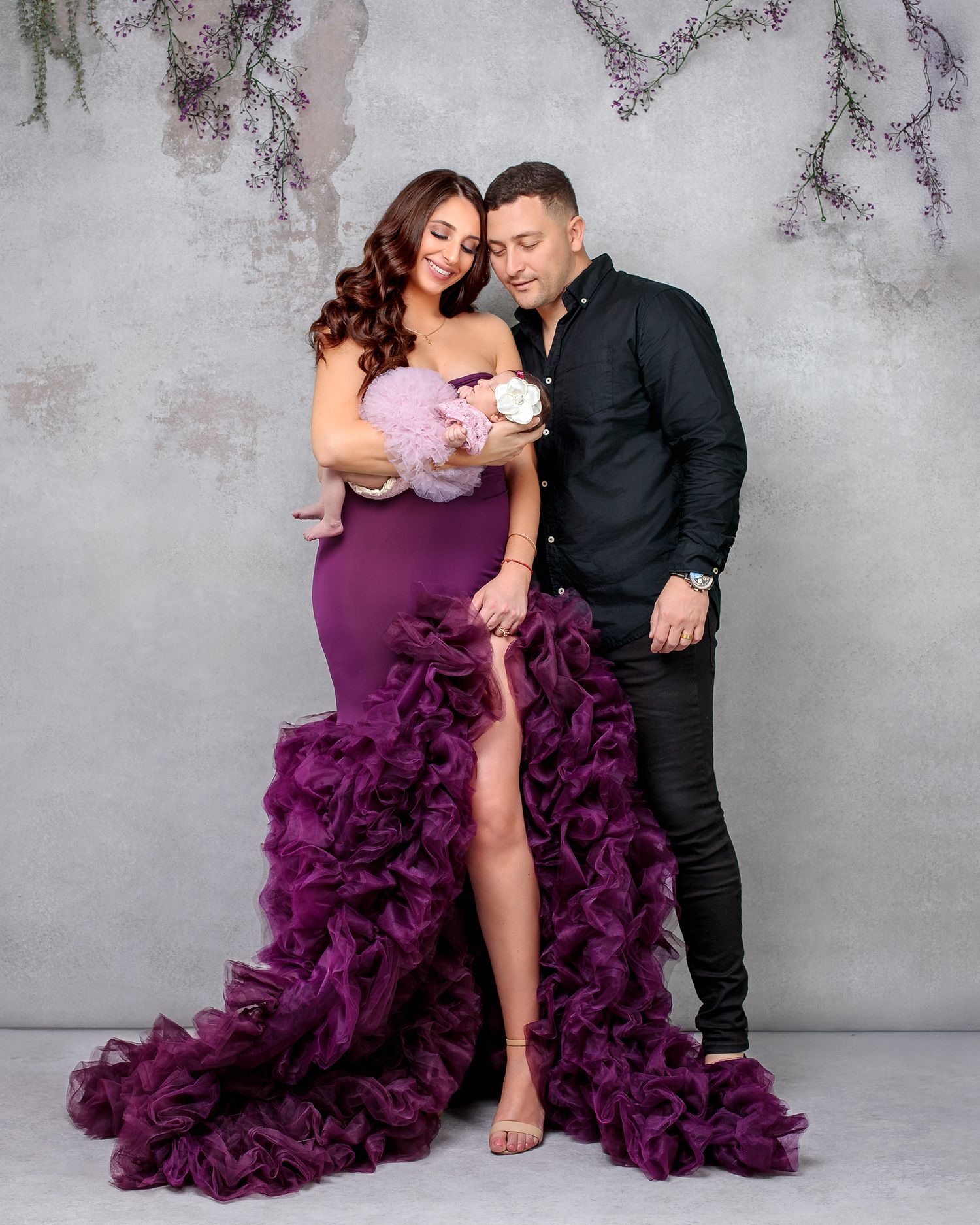 Couple smiling both looking at their newborn baby girl all looking smart in designer studio client wardrobe provided by Caz Captures.