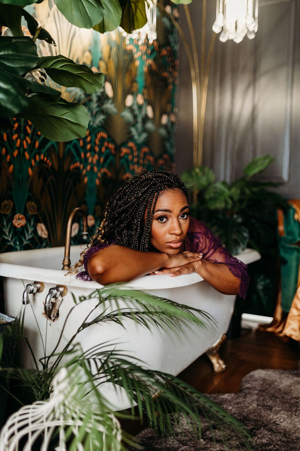 Woman with box braids relaxing in a clawfoot bathtub surrounded by lush tropical plants in a botanical bathroom.