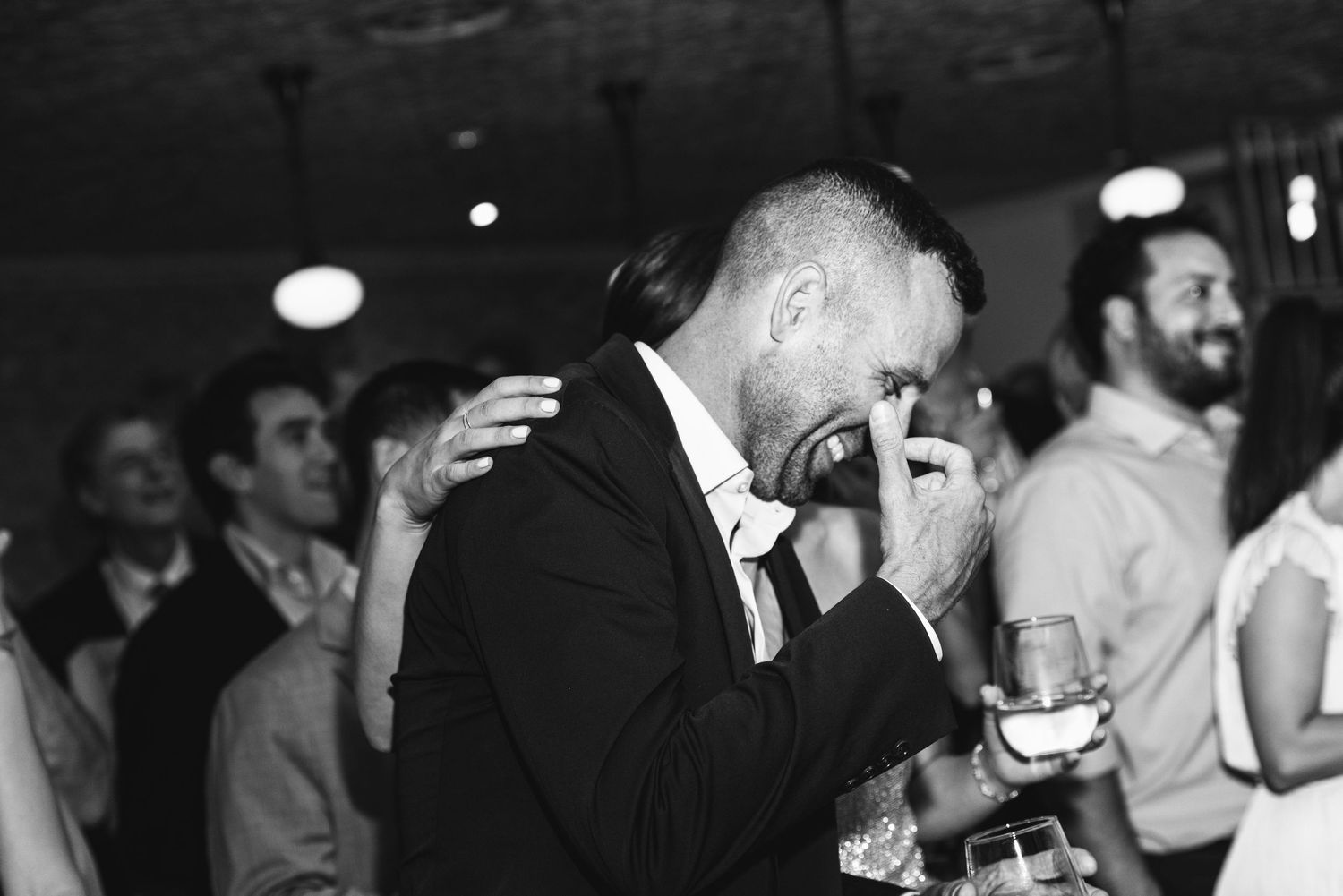 black and white candid photograph of groom laughing at wedding