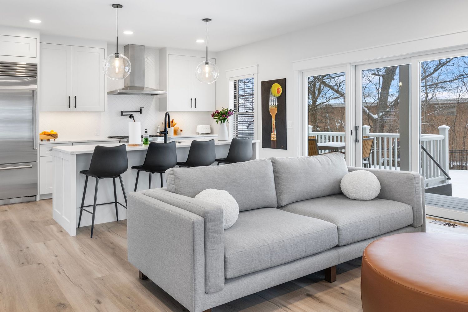 Modern open concept kitchen and living room with light gray sofa, hardwood floors and sliding glass doors to deck.