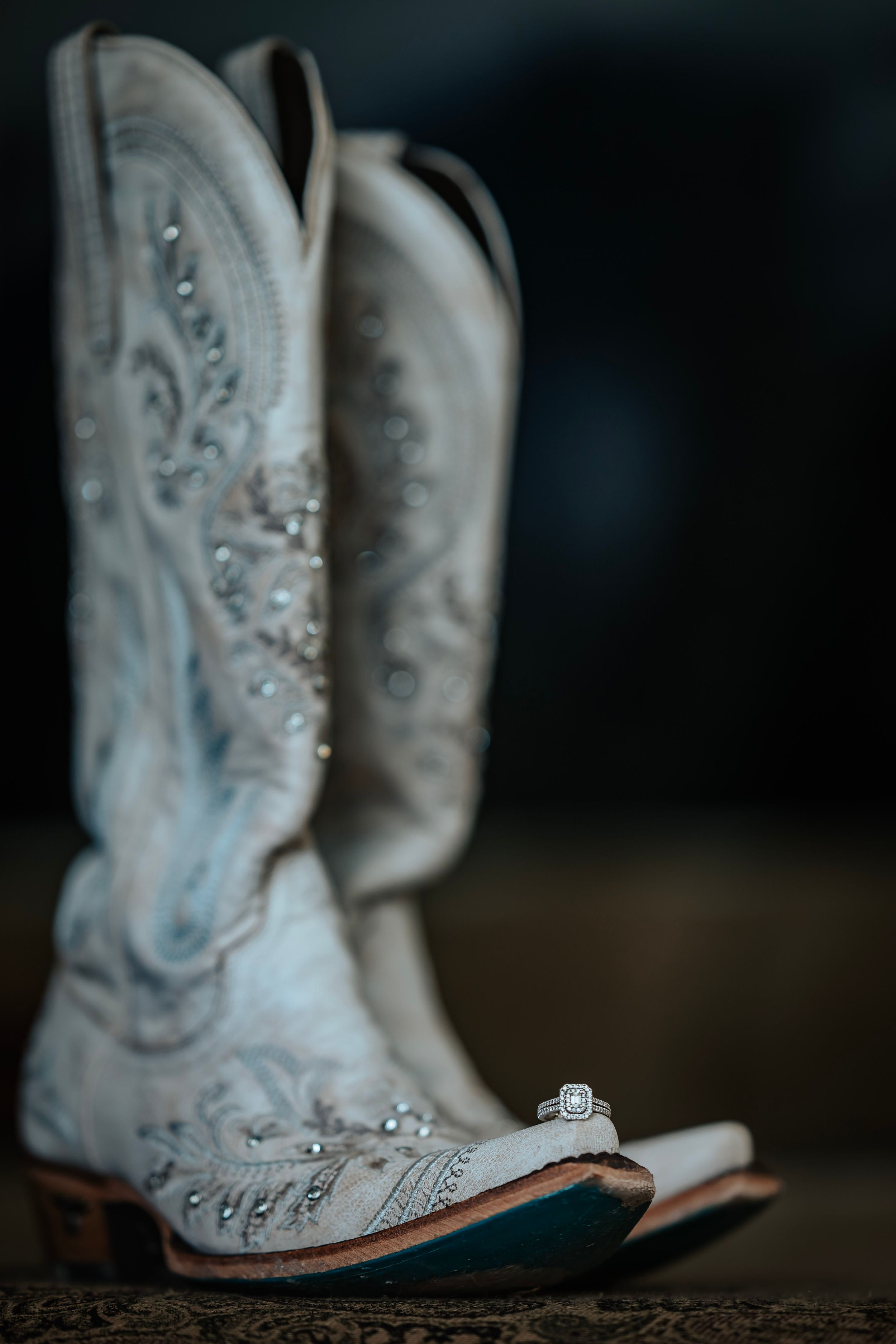 White embroidered cowboy boots with a diamond engagement ring placed on the toe in rustic wedding detail shot.